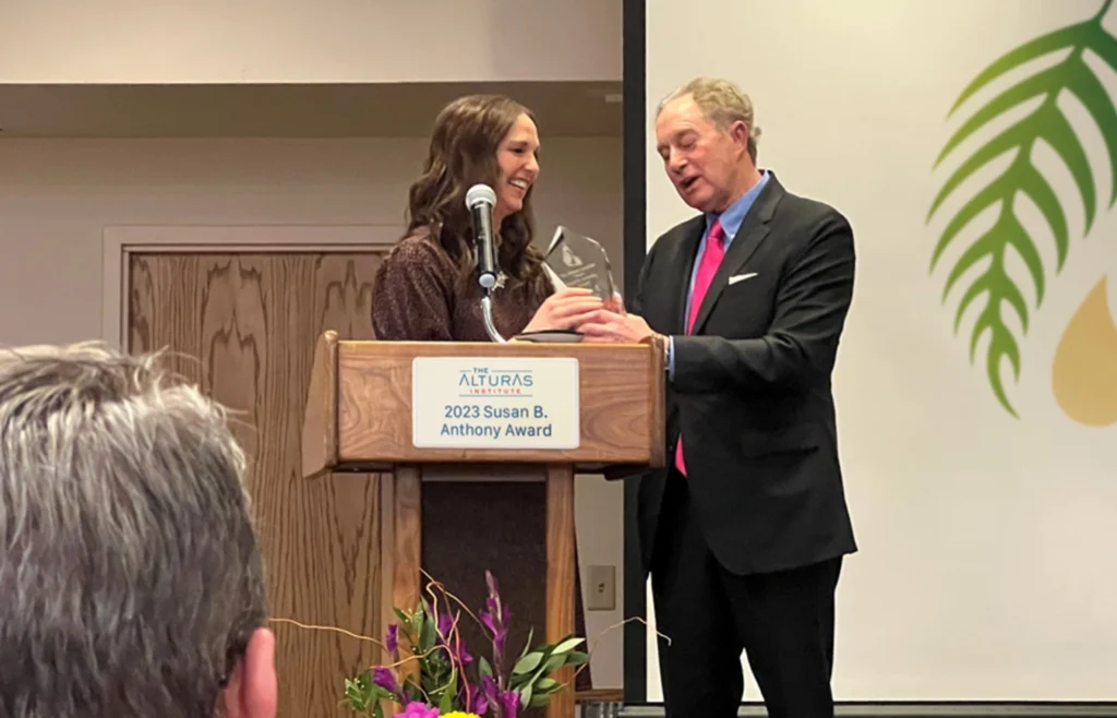Melaleuca CHRO Jamie Reynolds stands at a podium to accept the Susan B. Anthony Award from David Adler of the Alturas Institute.