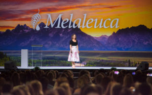 women on a stage with Melaleuca logo behind her